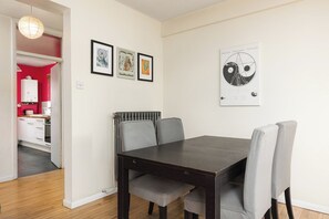 A dining area with a dark wooden table and grey upholstered chairs, a radiator, and framed artwork on the wall. - New! Characterful 3BR Flat | Peckham Rye Park (Greater London)