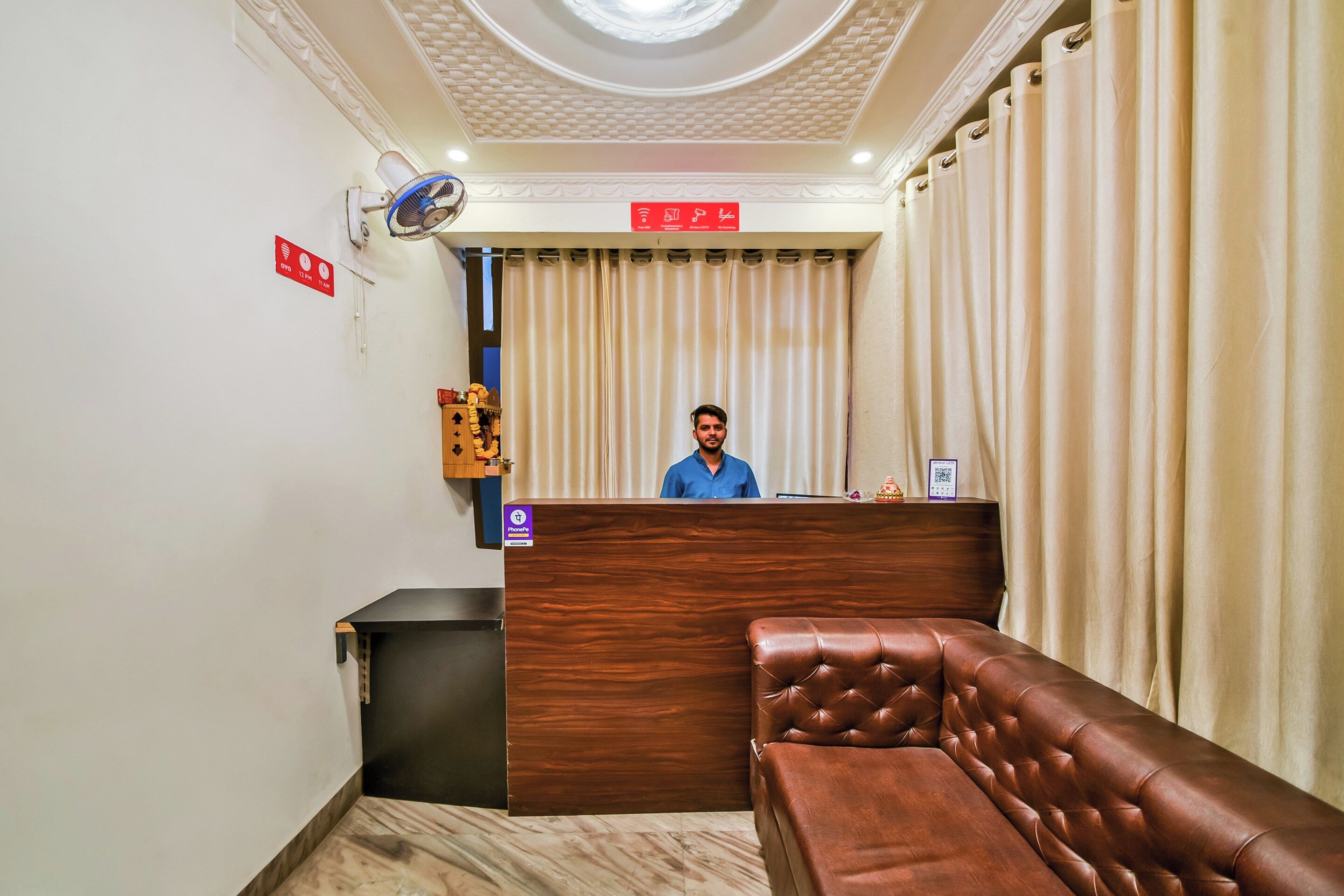 Zona de recepción de un hotel con un mostrador de madera, un sofá de cuero marrón y un ventilador de techo.