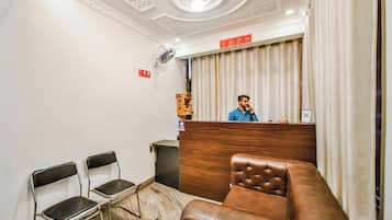 Zona de recepción de hotel con un mostrador de madera, un sofá de cuero marrón y dos sillas de metal.