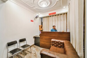 Zona de recepción de hotel con un mostrador de madera, un sofá de cuero marrón y dos sillas de metal.