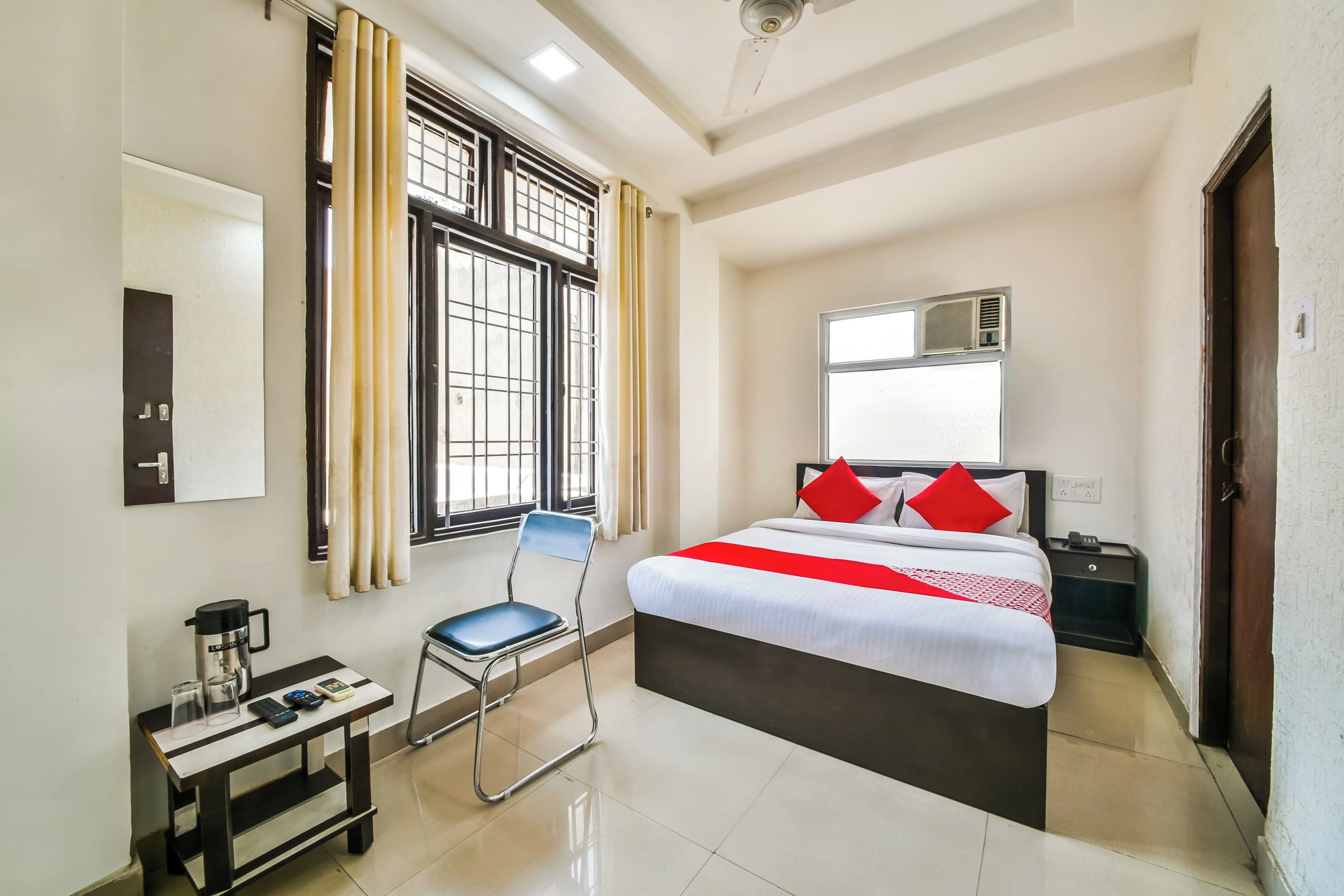 Una habitación de hotel con cama, escritorio, silla, ventana con cortinas y ventilador de techo.
