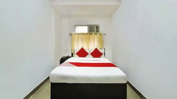 Habitación de hotel estrecha con cama, mesita de noche, teléfono y unidad de aire acondicionado en la pared.