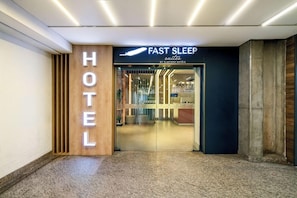 Entrada de hotel con un letrero que dice 'FAST SLEEP SUITES BY SLAVIERO HOTELS' y un panel de madera con la palabra 'HOTEL' iluminada.