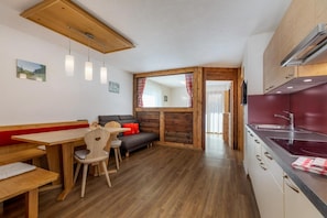 Una cucina accogliente con mobili in legno, un'area pranzo con una panca e sedie, e vista sul soggiorno attraverso una finestra.