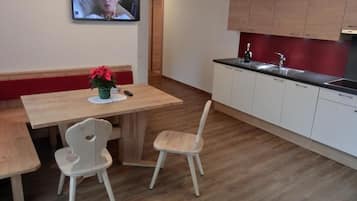 Una cucina moderna con mobili in legno, un tavolo da pranzo con due sedie e una televisione montata a parete.