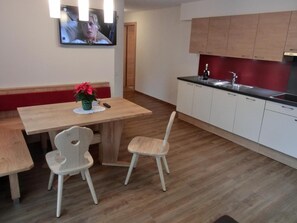 Una cucina moderna con mobili in legno, un tavolo da pranzo con due sedie e una televisione montata a parete.