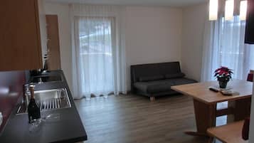 Eine moderne Küche mit Spüle und Flasche, ein graues Sofa, ein Holzesstisch mit Pflanze und ein Fenster mit Vorhängen.