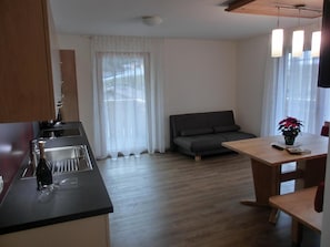 Una cucina moderna con lavello e una bottiglia, un divano grigio, un tavolo da pranzo in legno con una pianta e una finestra con tende.
