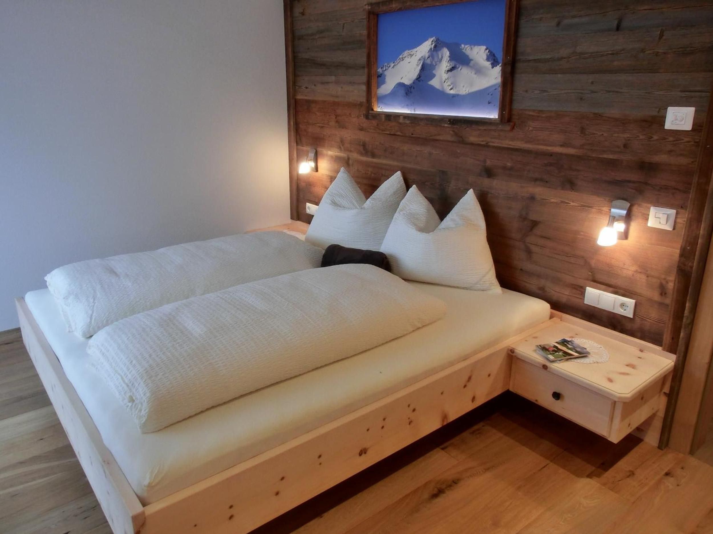 Un letto con testiera in legno, numerosi cuscini e un comodino con una lampada.