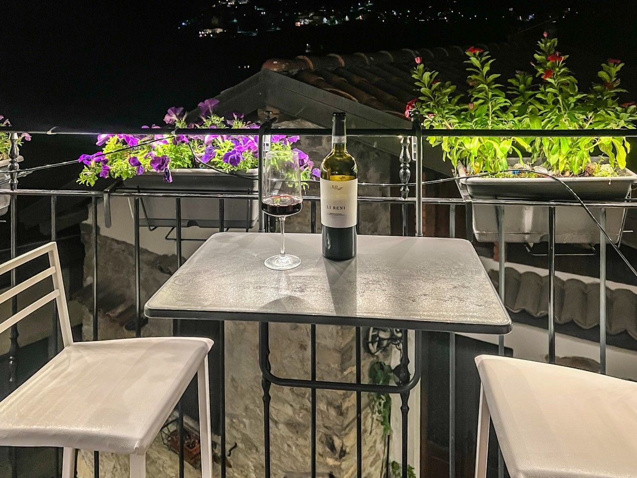 Ein Balkon mit Tisch, zwei Stühlen, einer Weinflasche und Topfpflanzen.