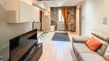 Un salon équipé d’un téléviseur à écran plat, d’un canapé, d’une table basse et d’un mur en pierre en arrière-plan.