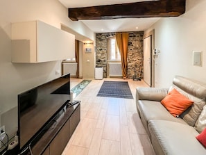 Ein Wohnzimmer mit Flachbildfernseher, einer Couch, einem Couchtisch und einer Steinwand im Hintergrund.