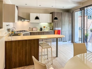 Une cuisine moderne dotée d’un îlot central, de luminaires suspendus et offrant une vue sur l’extérieur.