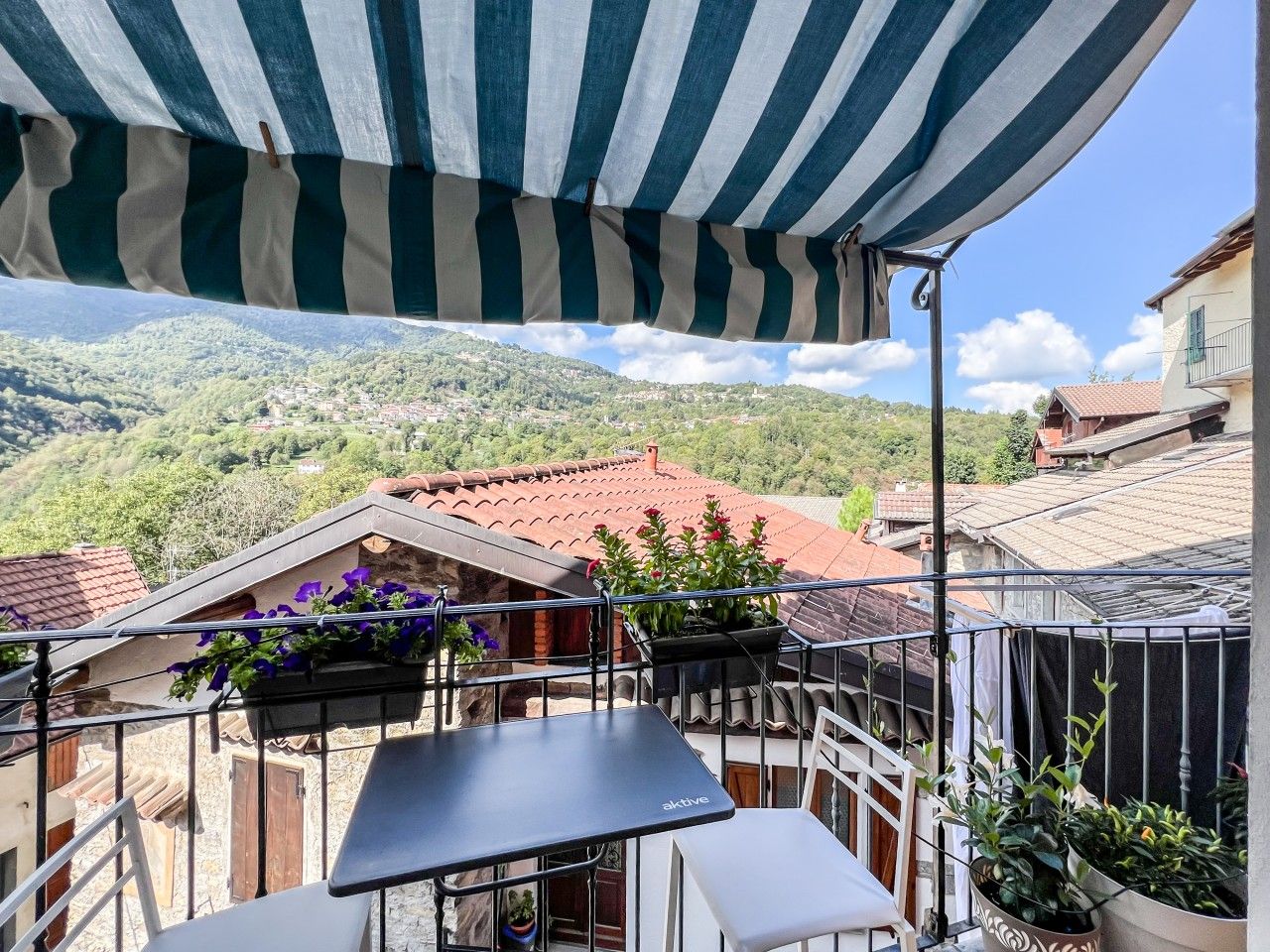 Un balcon donnant sur un village, une table et des plantes en pot.