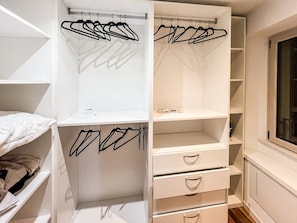 Ein Schlafzimmer mit einem Bett, einem weißen Kleiderschrank mit vielen Regalen und Schubladen sowie einem Fenster.