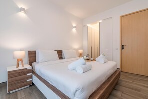 Una habitación de hotel moderna con una cama grande, lámparas de noche, una mesita de noche de madera, un armario de madera y suelo de madera.