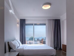 Una habitación de hotel con una cama, una mesita, una silla y vistas a la ciudad a través de un ventanal grande.