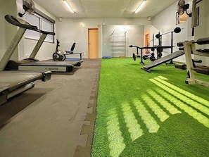 Un gimnasio con cintas de correr, una banca de pesas y una zona de césped artificial verde.