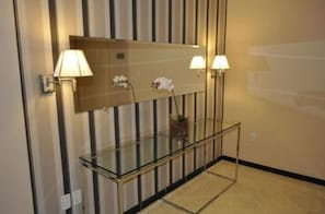 Un vestíbulo de hotel con una mesa consola de vidrio, dos lámparas de pared y un diseño de pared a rayas.