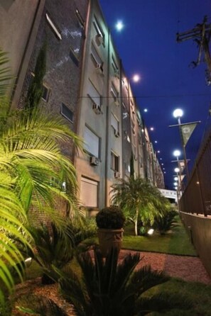 A nighttime view of a building with multiple floors, outdoor lighting, and some greenery.