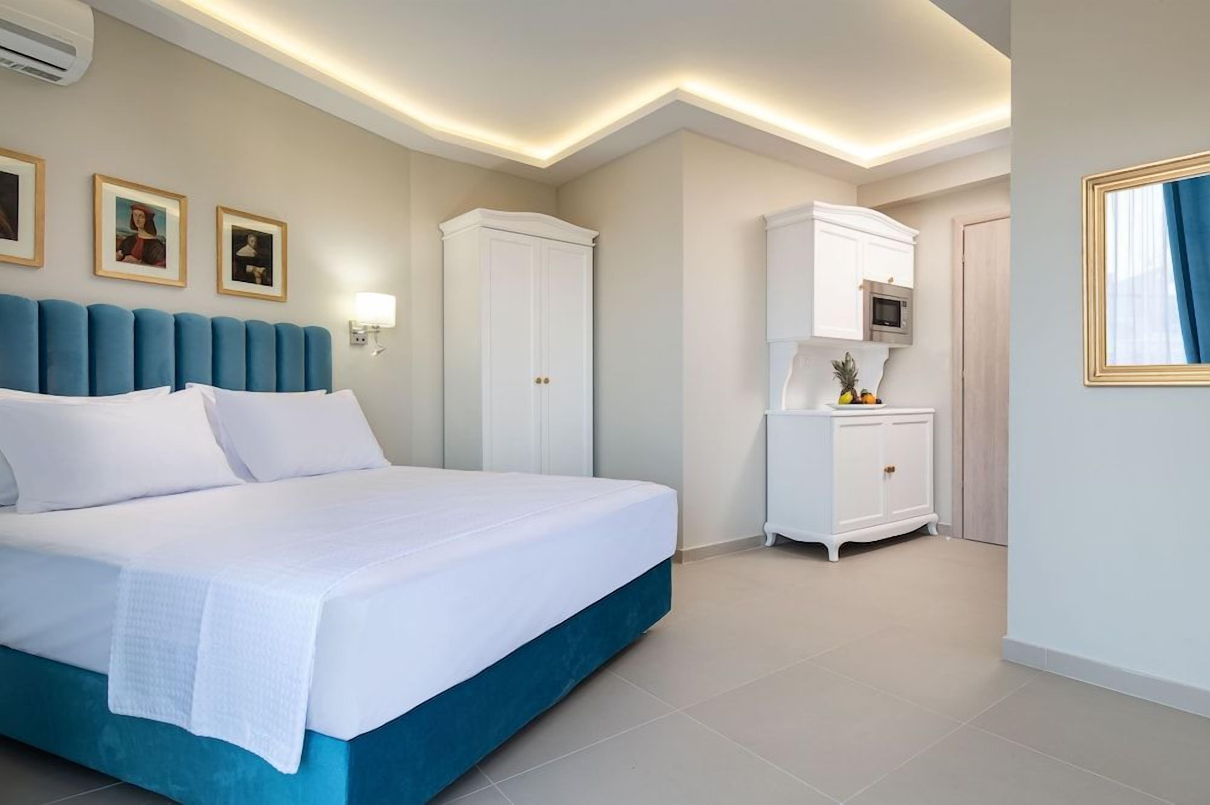 Una habitación de hotel con una cama grande, un armario, una mesita de noche con una lámpara y un televisor montado en la pared.