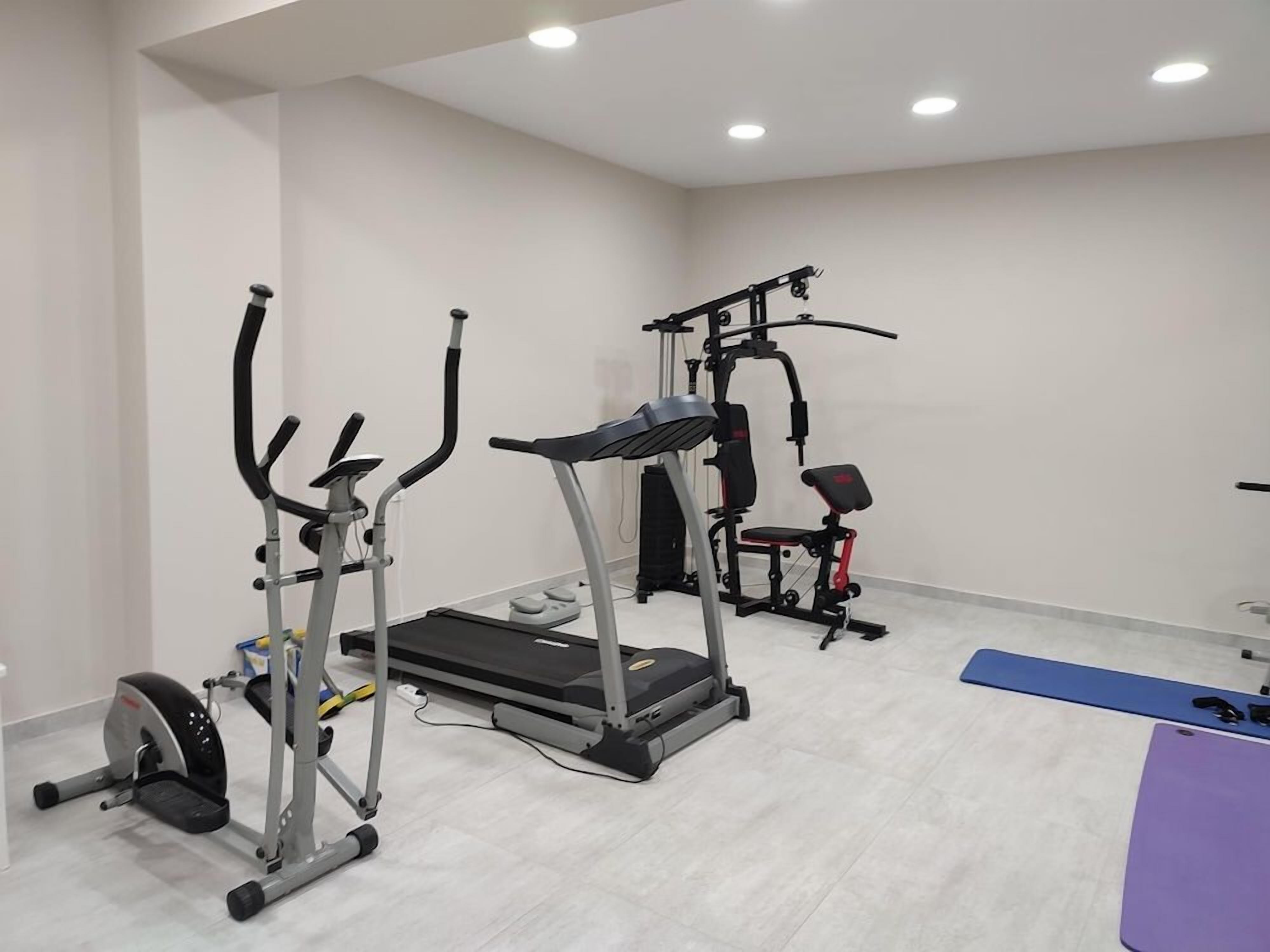 A gym with cardio equipment, a treadmill, and a bench.