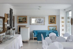 Uma sala de jantar com uma mesa comprida posta para refeição, um sofá azul e quadros nas paredes.