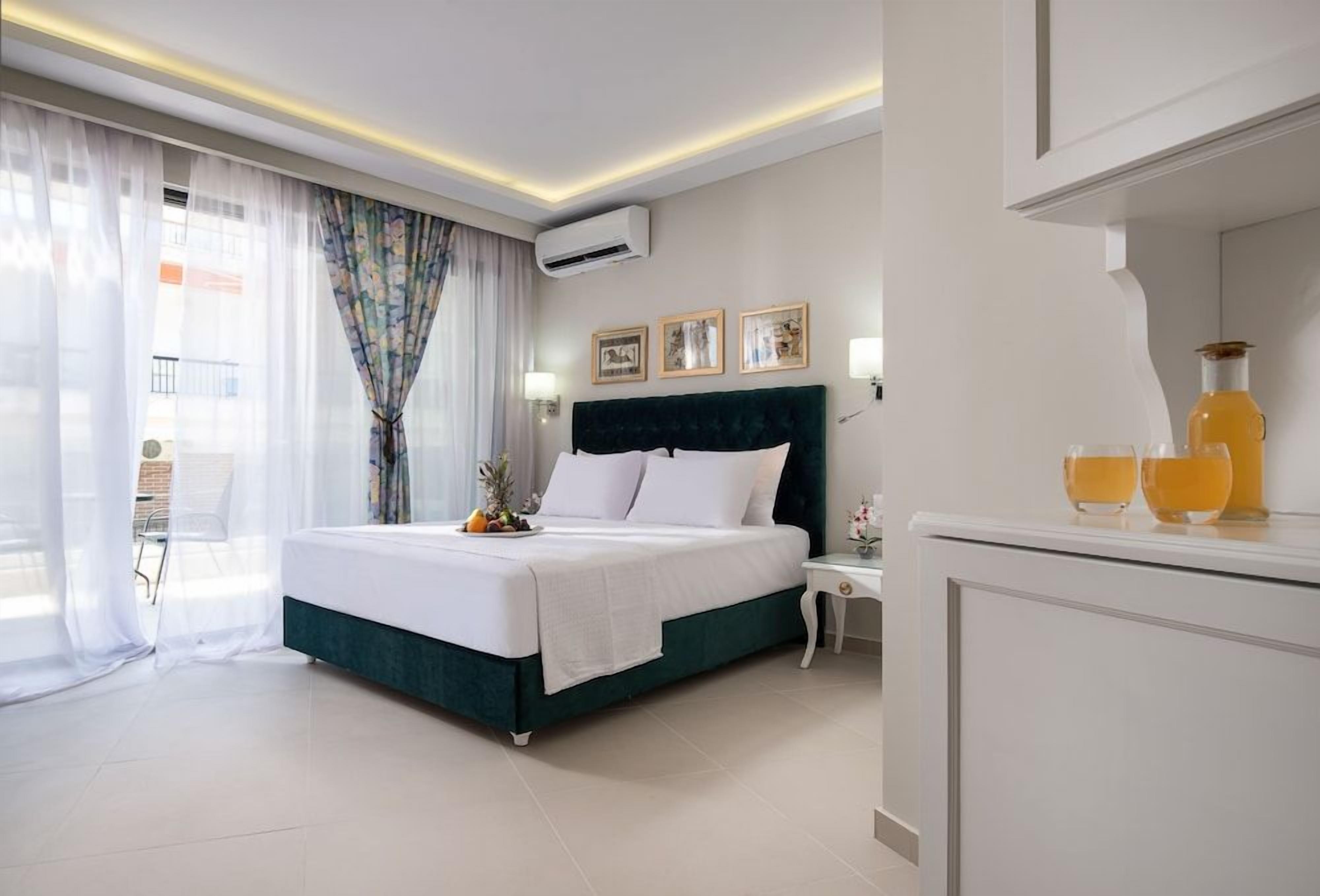 A hotel room with a bed, bedside table, lamp, air conditioning unit, and a view of the outside.