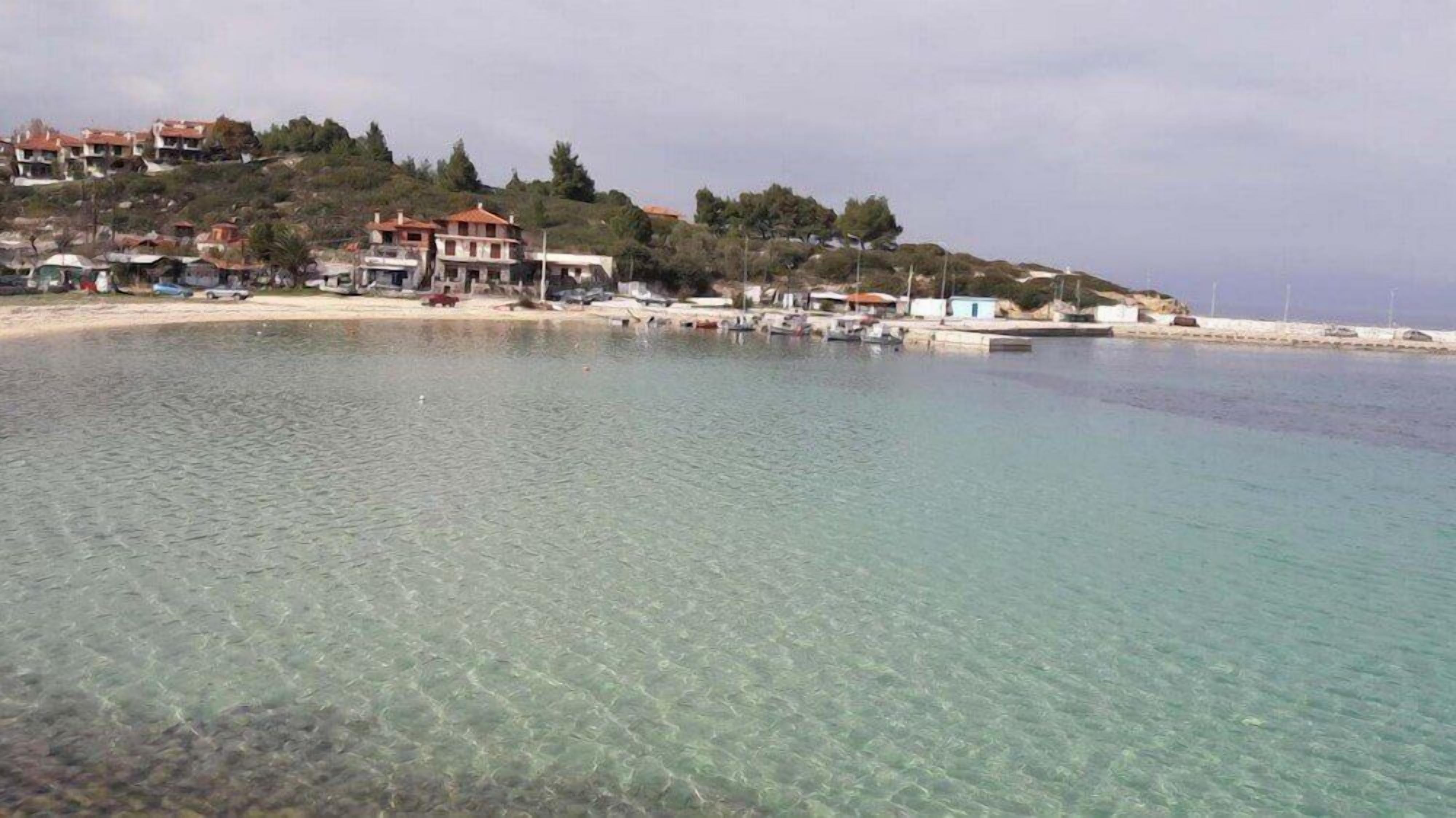 Una zona costera con aguas cristalinas, una playa arenosa y edificios en la ladera de una colina.