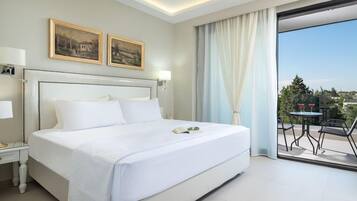 Habitación de hotel con una cama grande, una mesita de noche, una lámpara, dos cuadros en la pared y vistas al exterior a través de un ventanal.