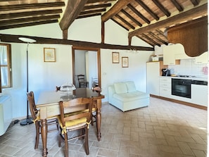 A dining area with a wooden table and chairs, a light-colored sofa, and a kitchen with white cabinets and appliances. - Vrbo Property (Camigliano)