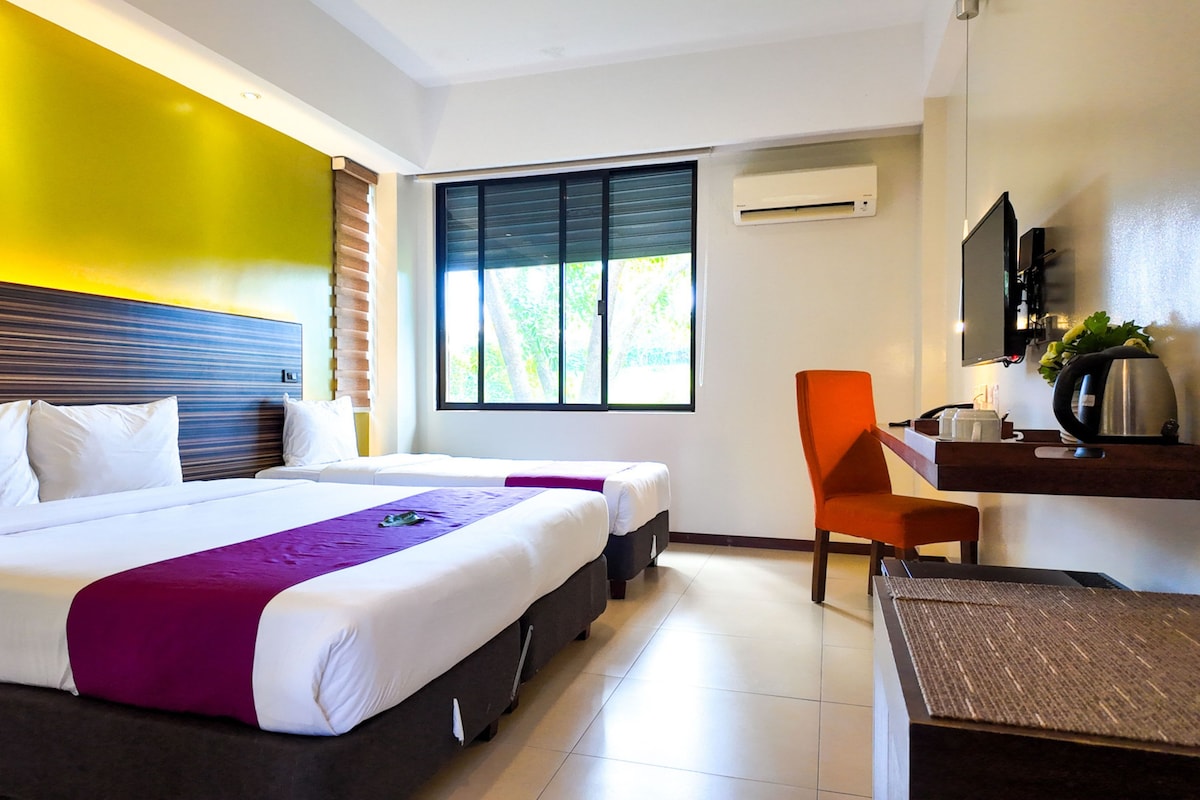 A hotel room with two beds, a desk, a chair, a television, and a window with blinds.