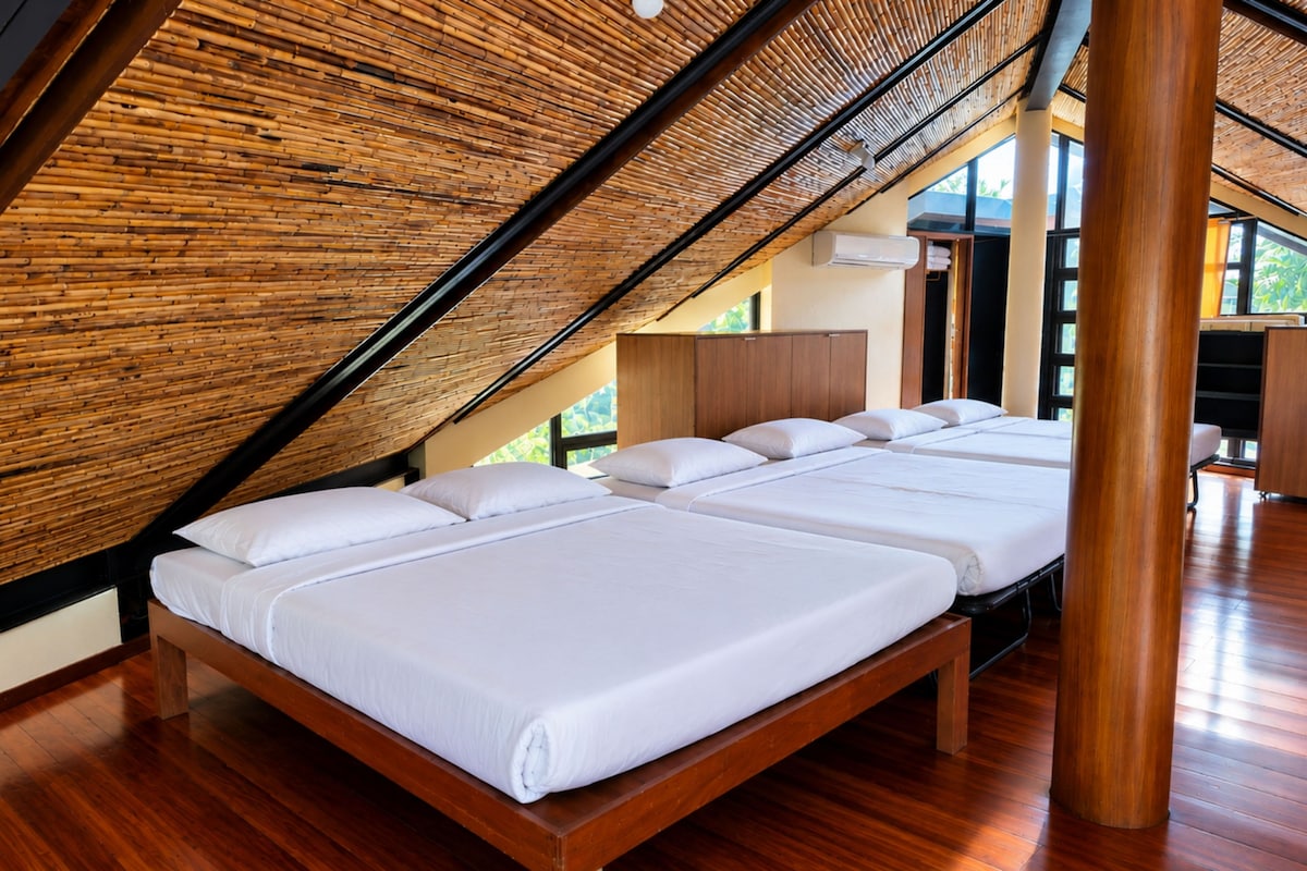 A room with a sloped ceiling, wooden flooring, and a bed with white bedding.