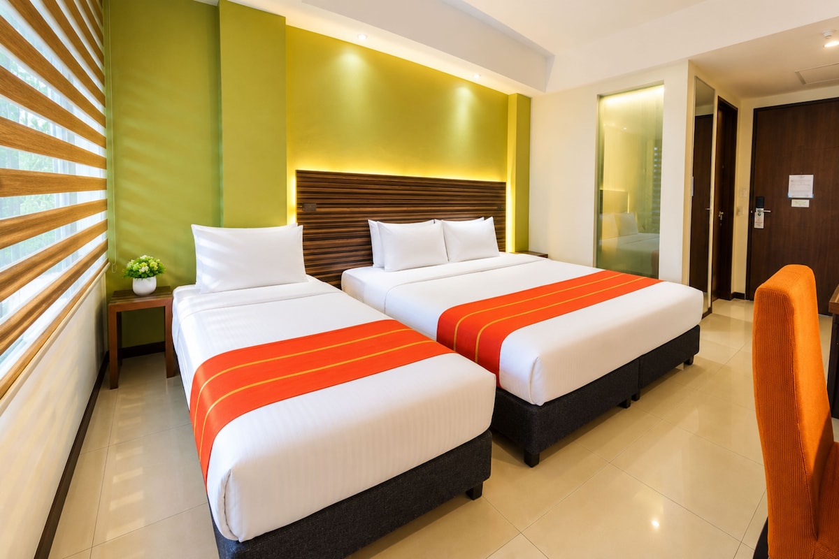 A hotel room with two beds, a nightstand, a small plant, and a wooden headboard.