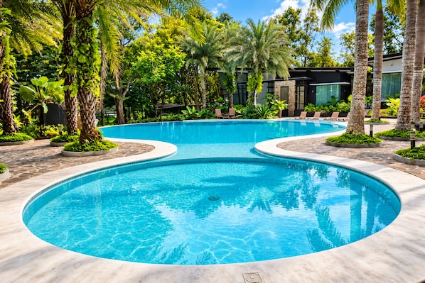 A swimming pool with a curved design, surrounded by palm trees and lush greenery.