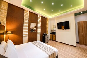 A modern hotel room with a bed, a flat-screen TV mounted on the wall, a small kitchenette, and a wooden wardrobe. - Abagatan ti Manila Hotel and Events Place Alfonso Tagaytay (Alfonso)
