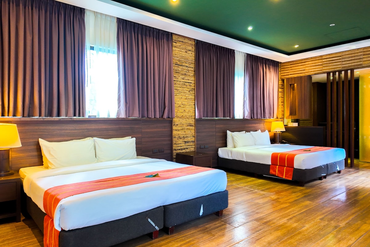 A hotel room with two beds, wooden flooring, and a large window with curtains.