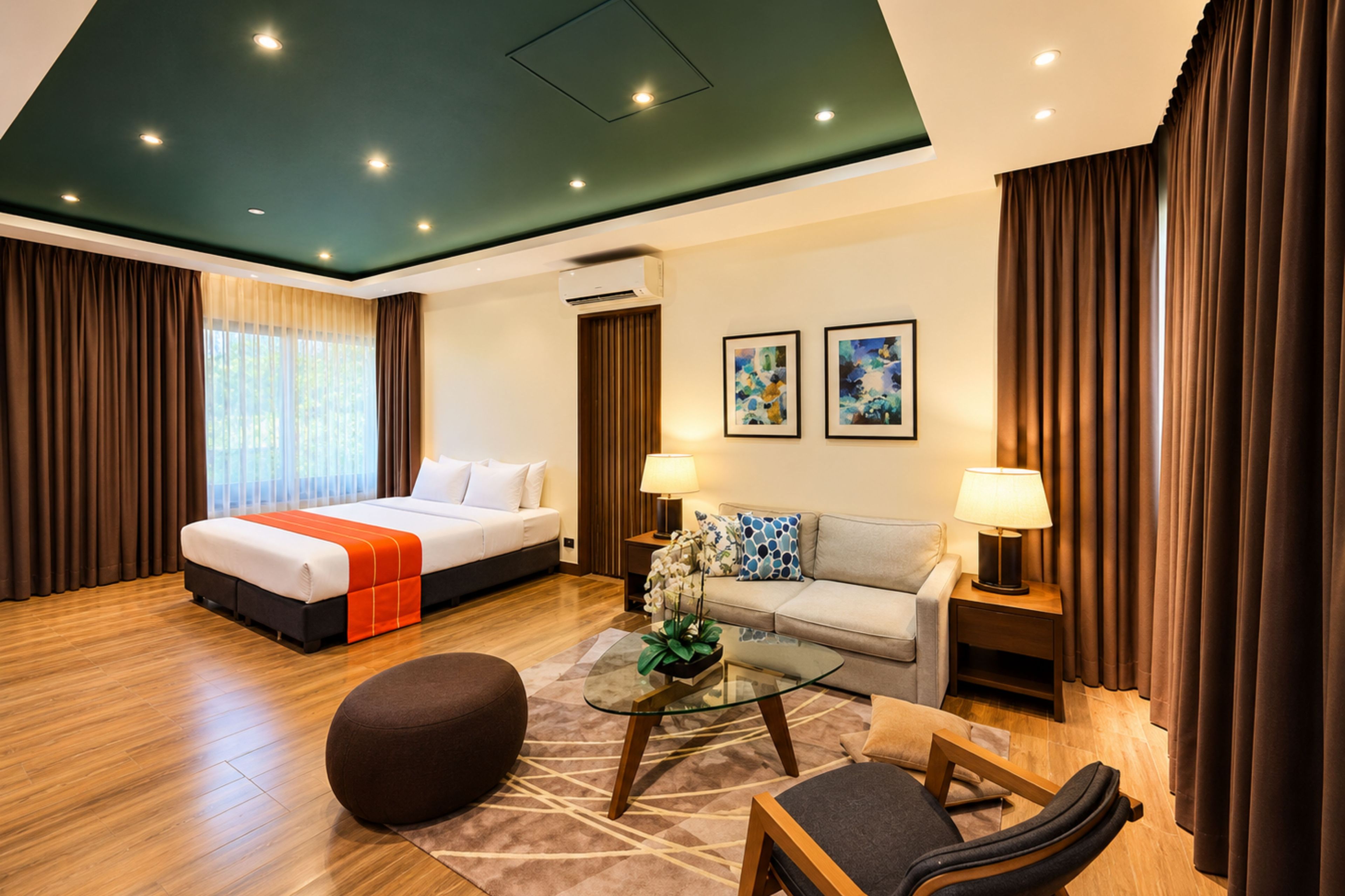 A hotel room with a bed, sofa, ottoman, coffee table, and artwork on the walls.