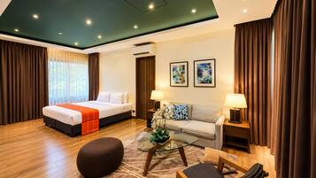 A hotel room with a bed, sofa, ottoman, coffee table, and artwork on the walls.