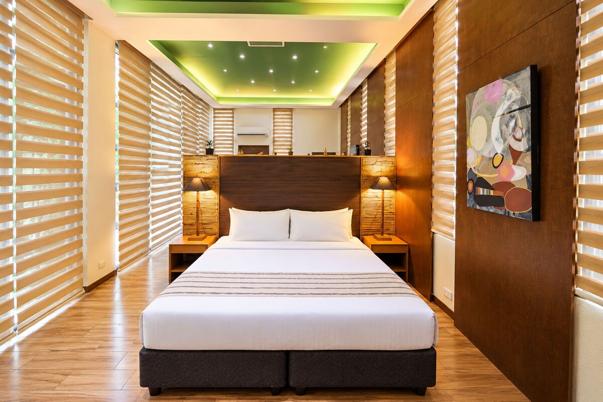 A hotel room with a large bed, wooden headboard, bedside lamps, and a painting on the wall.