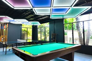 A pool table with a green felt surface, surrounded by walls with large windows and a ceiling with geometric light fixtures. - Abagatan ti Manila Hotel and Events Place Alfonso Tagaytay (Alfonso)