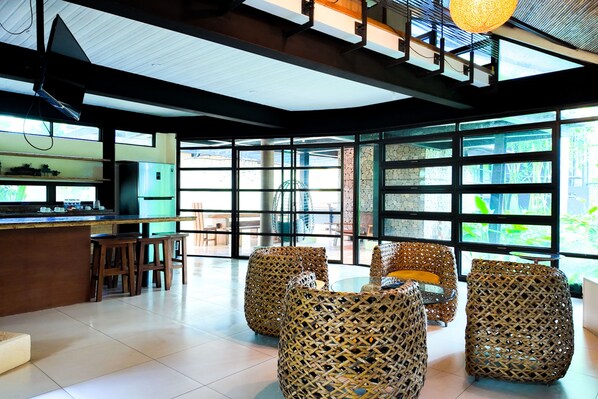 A spacious room with a large window, wicker furniture, and a kitchen area. - Abagatan ti Manila Hotel and Events Place Alfonso Tagaytay (Alfonso)