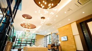 A modern hotel lobby with a large seating area, a reception desk, and a large window offering a view of the outdoors.