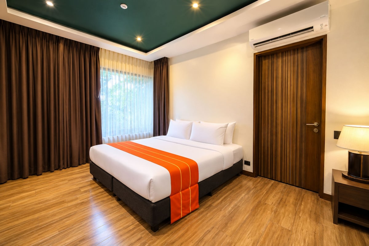 A hotel room with a bed, curtains, an air conditioning unit, and a lamp.
