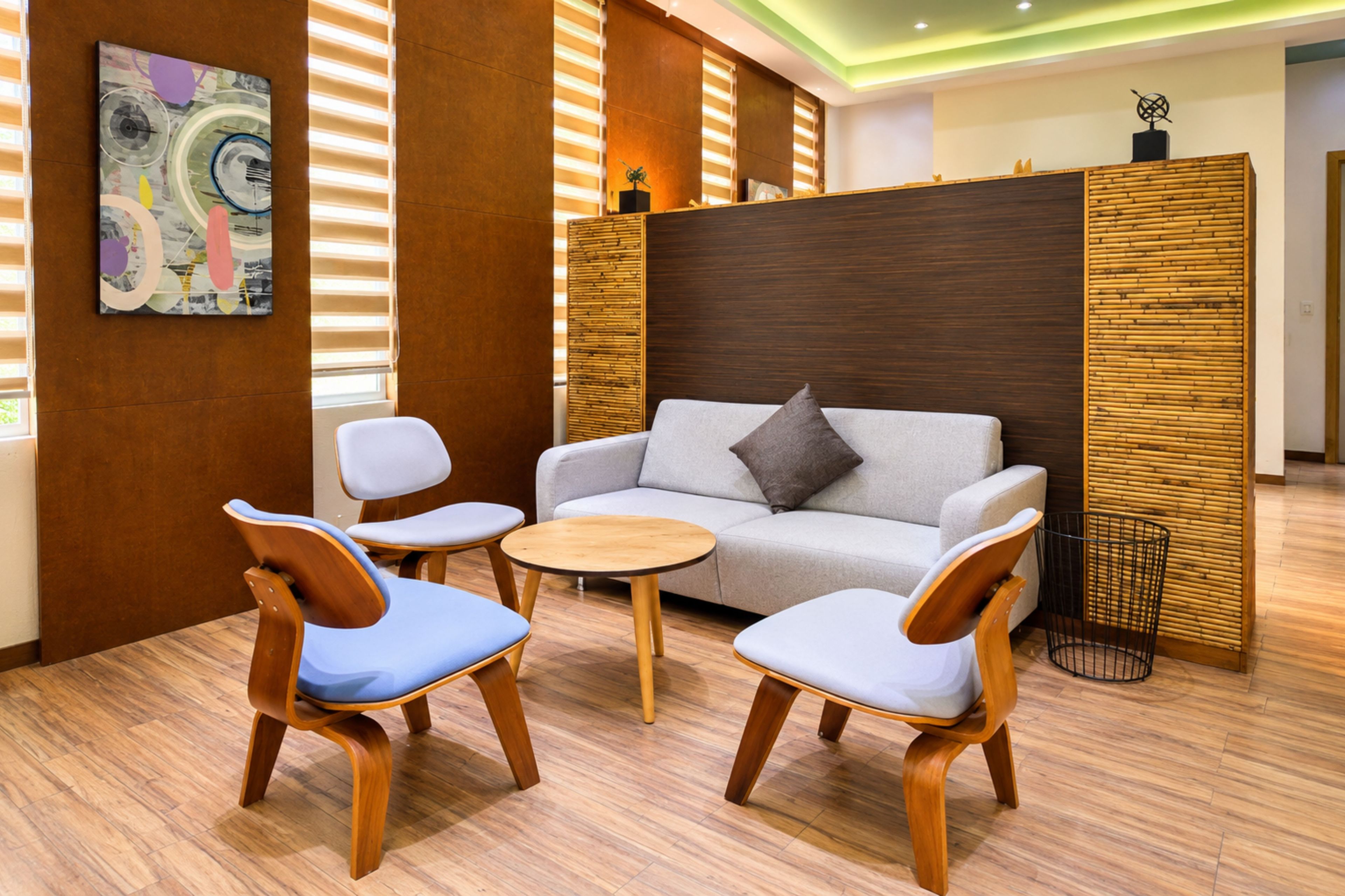 A modern living room with a sofa, two chairs, a small round table, and a decorative wall piece.