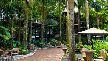 An outdoor patio area with brick flooring, wicker furniture, and lush greenery.