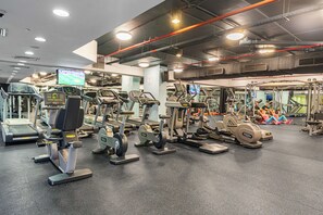 Ein Fitnessstudio mit verschiedenen Trainingsgeräten, darunter Laufbänder und Crosstrainer, die in Reihen angeordnet sind.