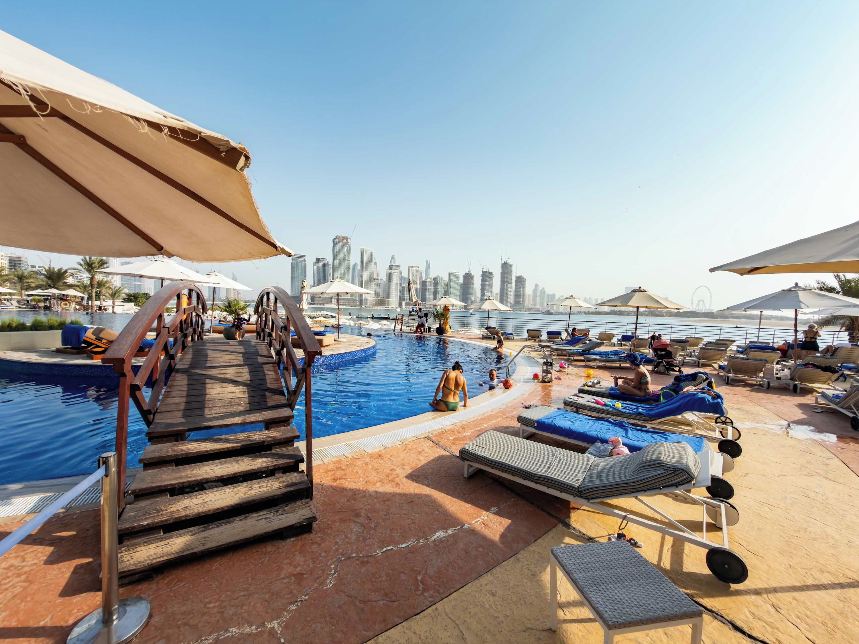 Un espace piscine doté d’une terrasse en bois, de chaises longues et de parasols.