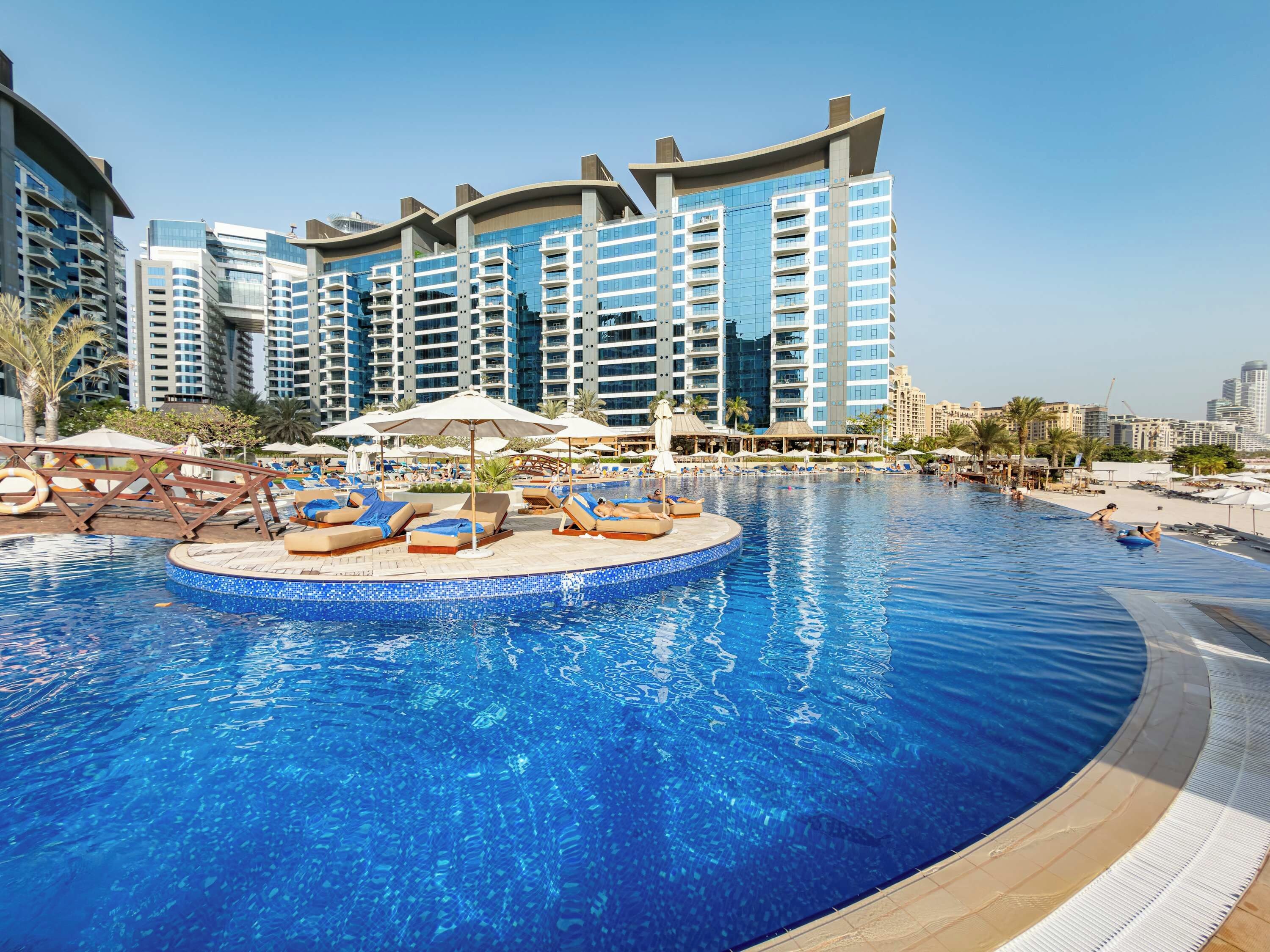 A swimming pool with lounge chairs and umbrellas, surrounded by high-rise buildings.