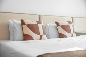 Ein Bett mit Kopfteil, zwei Kissen mit geometrischem Muster und einer weißen Bettdecke.
